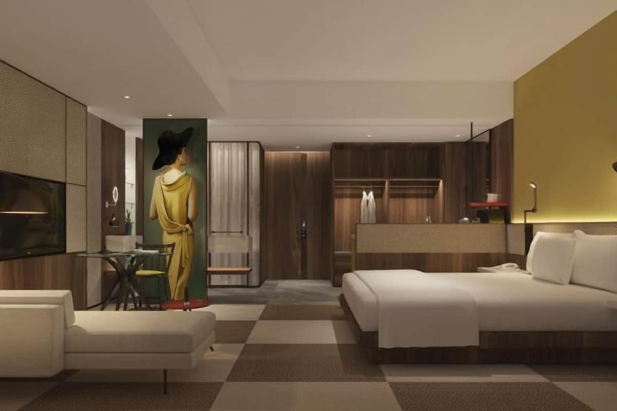 A modern hotel room with a bed, seating area, and a wardrobe.