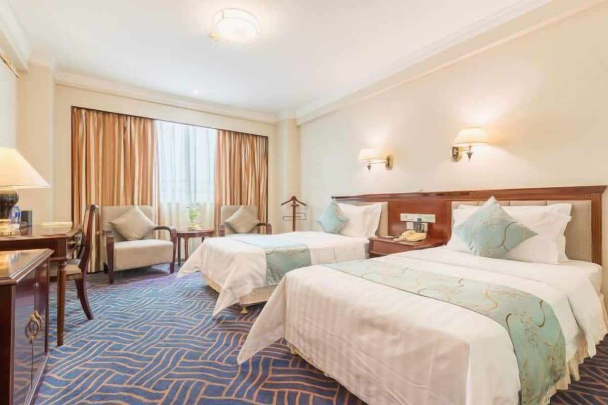 A hotel room with two beds, a desk, a chair, and a large window with curtains.