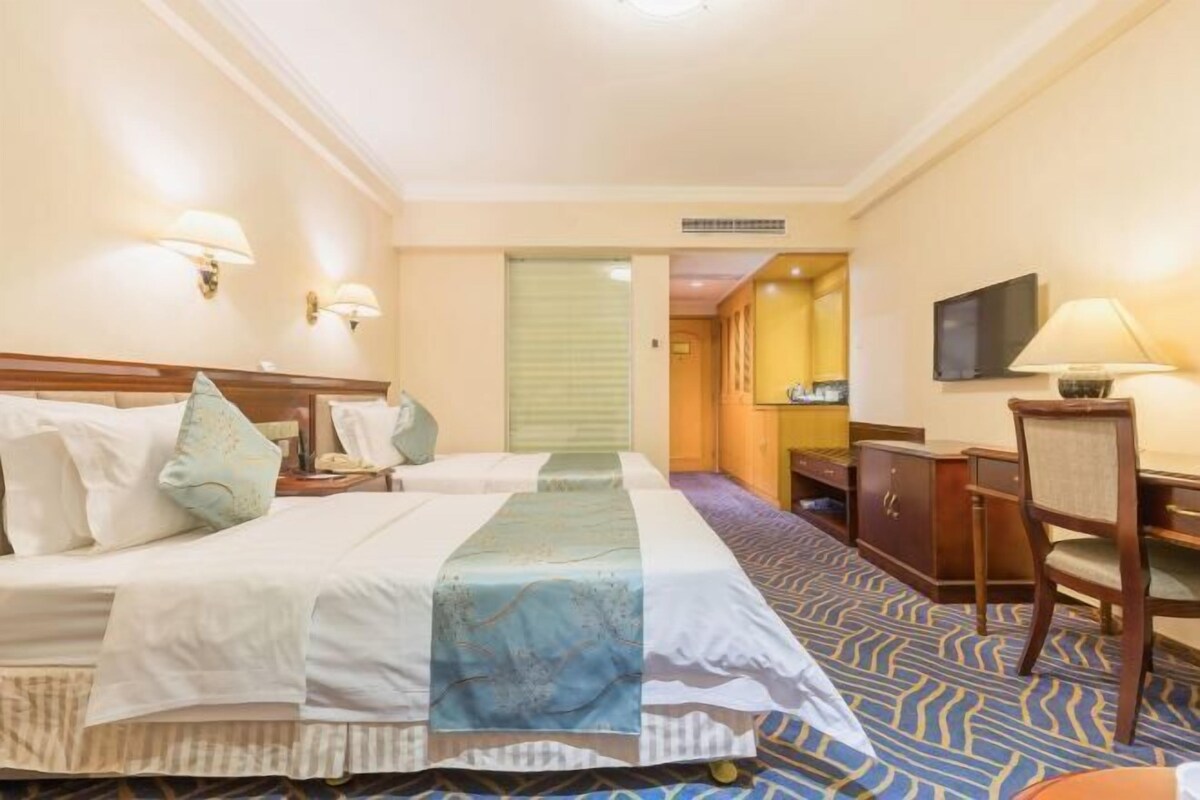 Une chambre d’hôtel avec deux lits, un bureau, une chaise, une télévision et une salle de bain visible à travers une porte.
