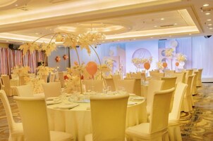 A banquet hall with round tables, chairs, and floral centerpieces.