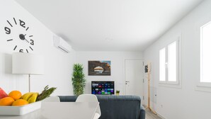 Ein modernes Wohnzimmer mit einer Couch, einem Esstisch, einer Wanduhr, einem Fernseher und einem Fenster.