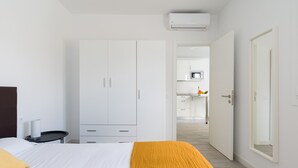 Ein modernes Schlafzimmer mit einem großen Bett, einem Kleiderschrank und einem durchgehenden Gang erkennbaren Küchenbereich.