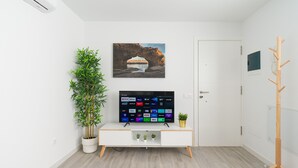 Ein modernes Wohnzimmer mit einem an der Wand befestigten Flachbildfernseher, einer weißen Unterhaltungsanlage mit Blumentopf und einem hölzernen Kleiderständer.