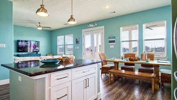 A kitchen with a large island, white cabinets, a dining area with wicker furniture, and a television on the left.