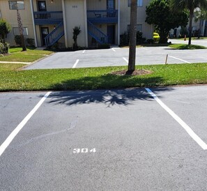A parking lot with marked spaces, a building with a blue staircase, and a tree casting a shadow. - Gulf Getaway #304 Free Beach Svc Chateau La Mer II 2nd Fl (Destin)