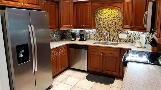 A kitchen with wooden cabinets, a stainless steel refrigerator, a dishwasher, and a tiled backsplash. - Gulf Getaway #304 Free Beach Svc Chateau La Mer II 2nd Fl (Destin)