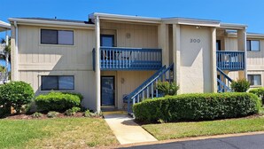 A two-story apartment building with a blue balcony on the second floor, a visible entrance, and a number '300' on the facade. - Gulf Getaway #304 Free Beach Svc Chateau La Mer II 2nd Fl (Destin)