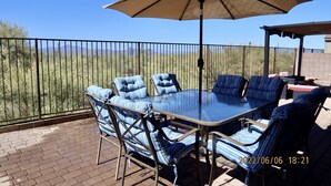 An outdoor patio with a glass table and striped chairs, a beige umbrella, and a view of a desert landscape. - Relax with Sonoran Nature Preserve views plus bike trails & several golf courses (Marana)