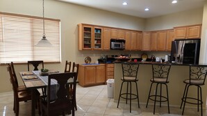 A kitchen with wooden cabinets, a microwave, a refrigerator, a dining table with chairs, and a bar area with stools. - Relax with Sonoran Nature Preserve views plus bike trails & several golf courses (Marana)
