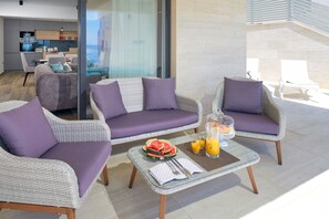 A modern living room with a glass coffee table, two grey sofas with purple cushions, and a view of a cityscape through large windows.