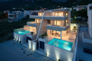 A modern multi-story house with a rooftop pool, outdoor seating, and a staircase leading to the upper levels.