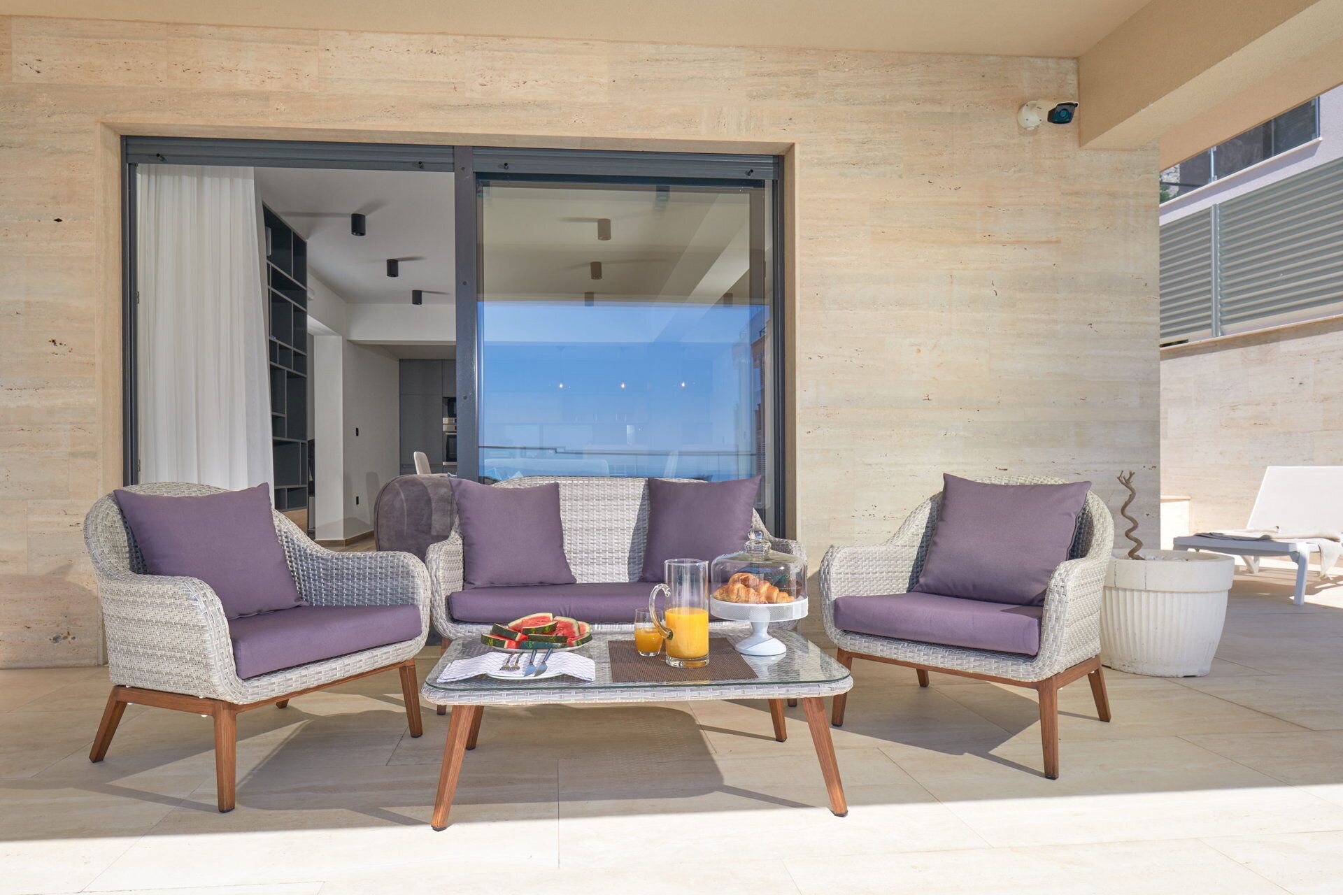 Un balcon avec des fauteuils en osier et une table en verre, dressée pour le petit-déjeuner.