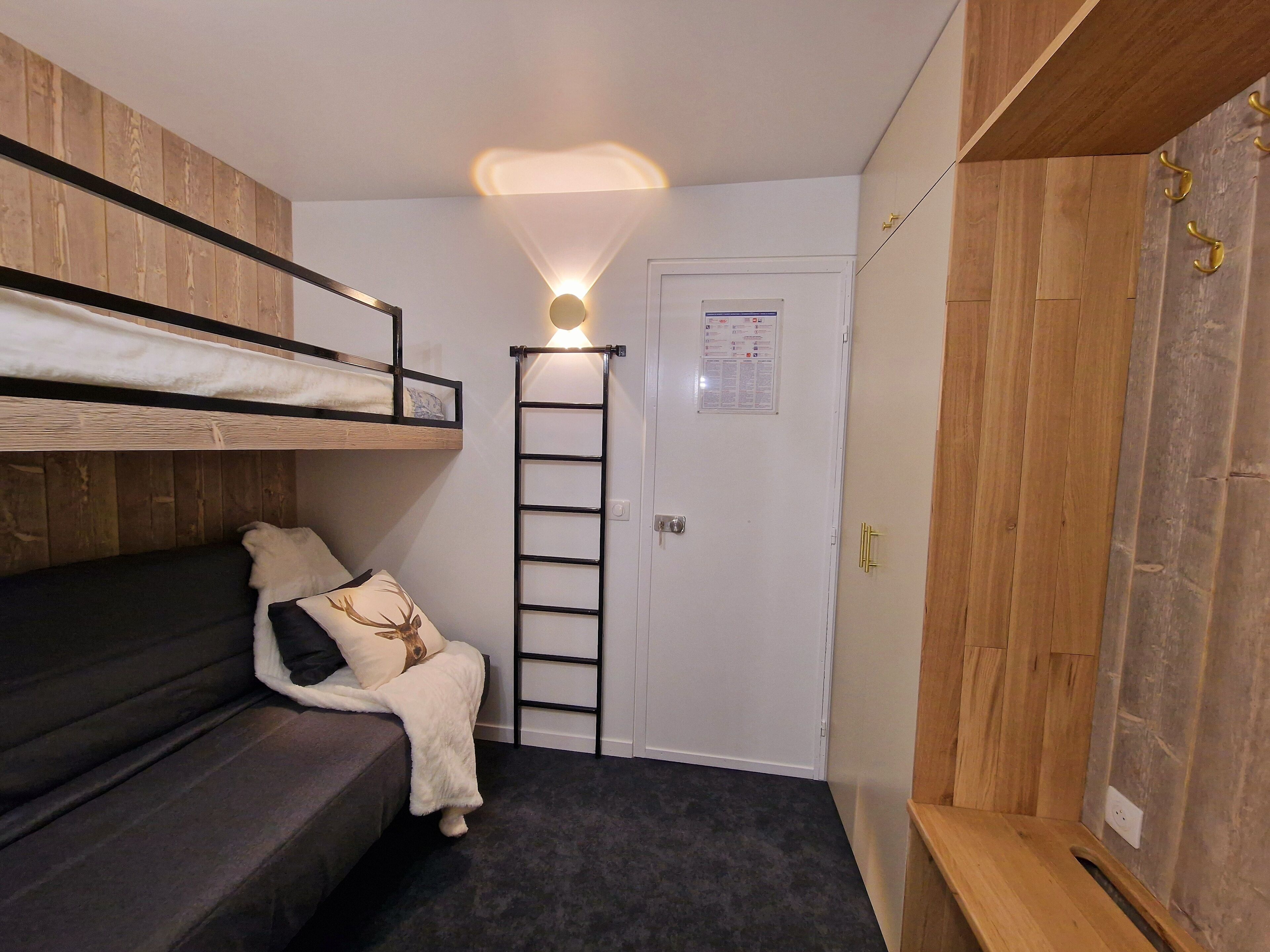 Une petite pièce avec un lit superposé, une échelle, une porte sur laquelle est affichée une note et un lambris en bois.