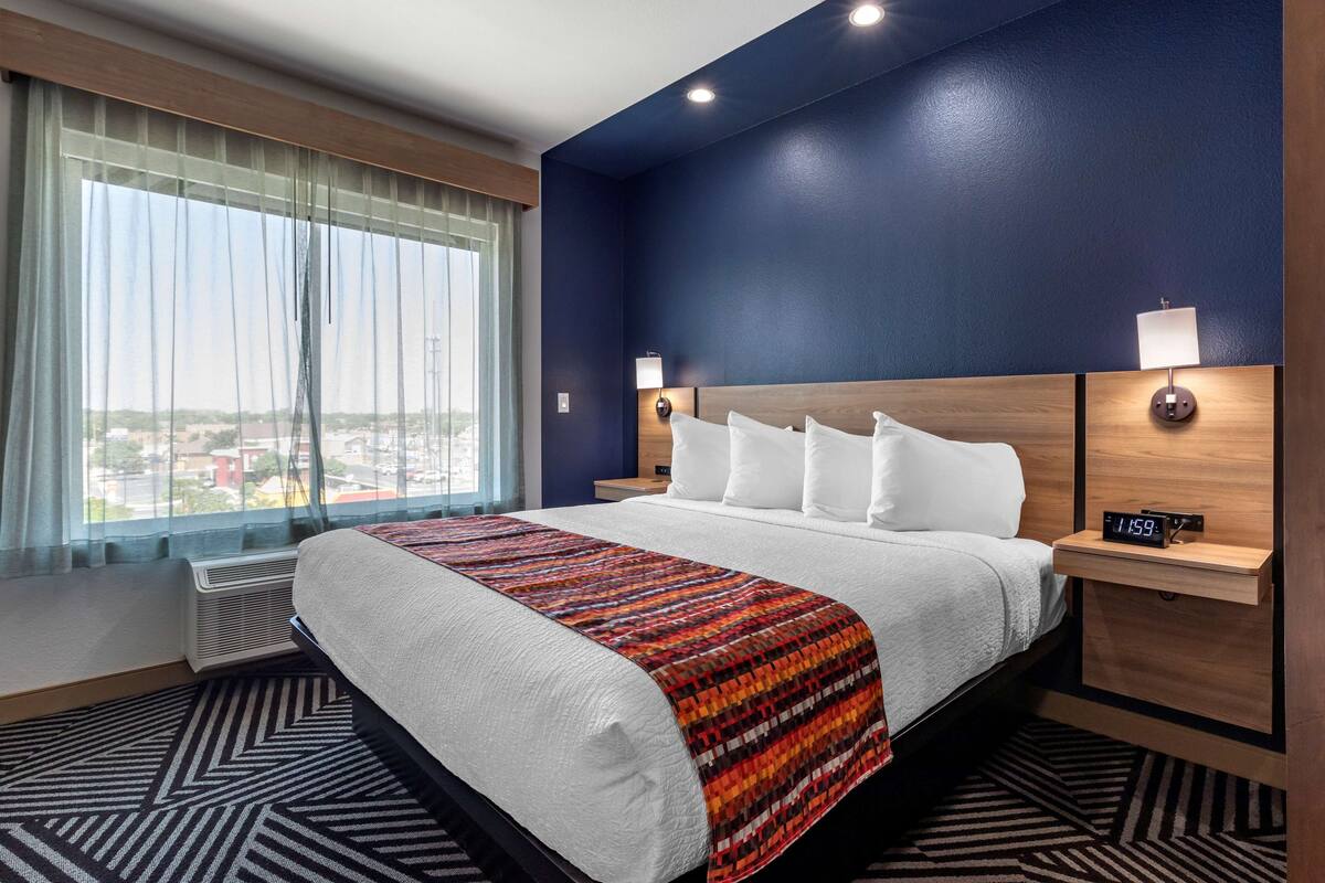 Een hotelkamer met een groot bed, stadszicht en een digitale klok op het nachtkastje.