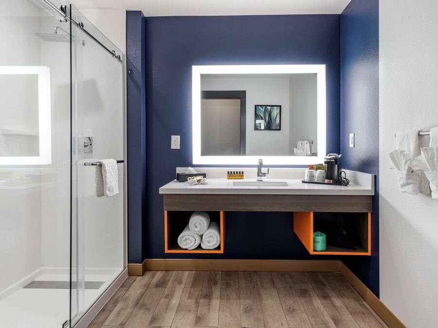 Une salle de bain moderne dotée d’une douche à parois de verre, d’un grand miroir et d’un meuble-lavabo en bois avec des rangements intégrés.