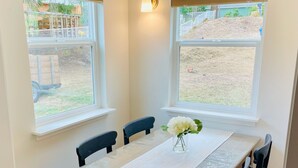 A dining area with a table set for four, two windows, and a light fixture on the wall. - Cottage of Tranquility (Bellingham)
