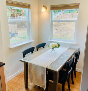 A dining area with a table set for four, two windows, and a light fixture on the wall.