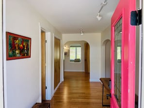A hallway with wooden flooring, a pink door, and a framed painting on the wall.