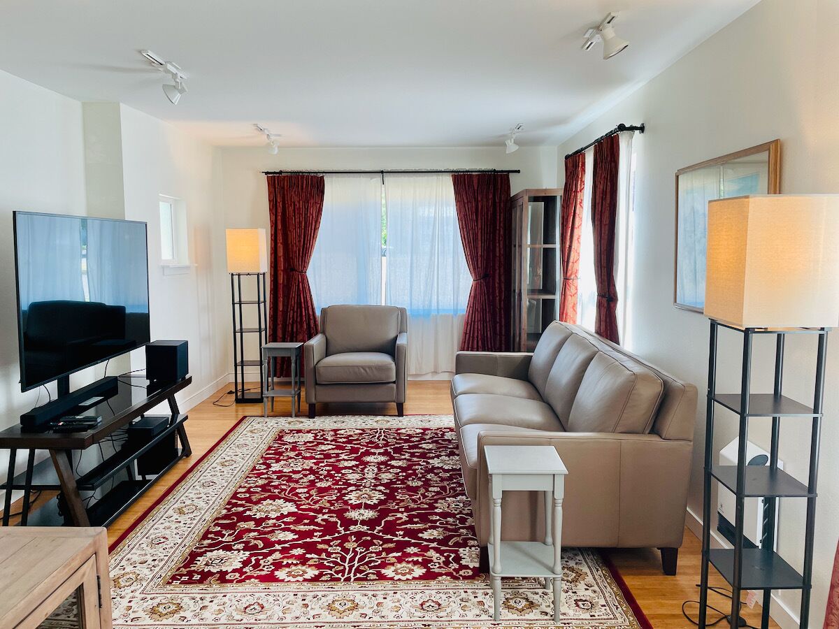 Uma sala de estar moderna com televisão de tela plana, um sofá cinza, um tapete estampado em vermelho e uma pequena mesa branca.