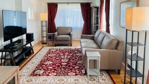 A modern living room with a flat-screen TV, a grey sofa, a red patterned rug, and a small white table. - Cottage of Tranquility (Bellingham)
