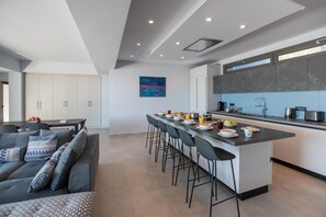 A modern kitchen with a central island, bar stools, and a dining area with a sofa and chairs.