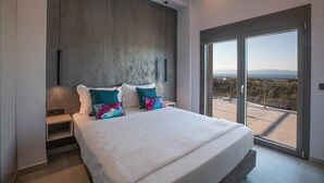 Een moderne slaapkamer met een groot bed, twee kussens, een nachtkastje en uitzicht door een schuifdeur naar buiten.