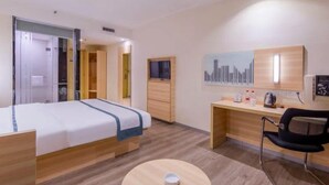 A hotel room with a bed, a desk, a chair, a round table, and a cityscape artwork on the wall. - City Comfort Inn (Liuzhou)