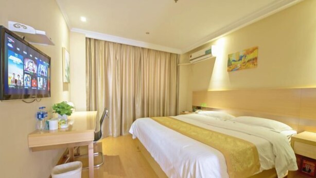 Habitació d'hotel amb un llit, un escriptori amb cadira, una televisió i una finestra amb cortines.