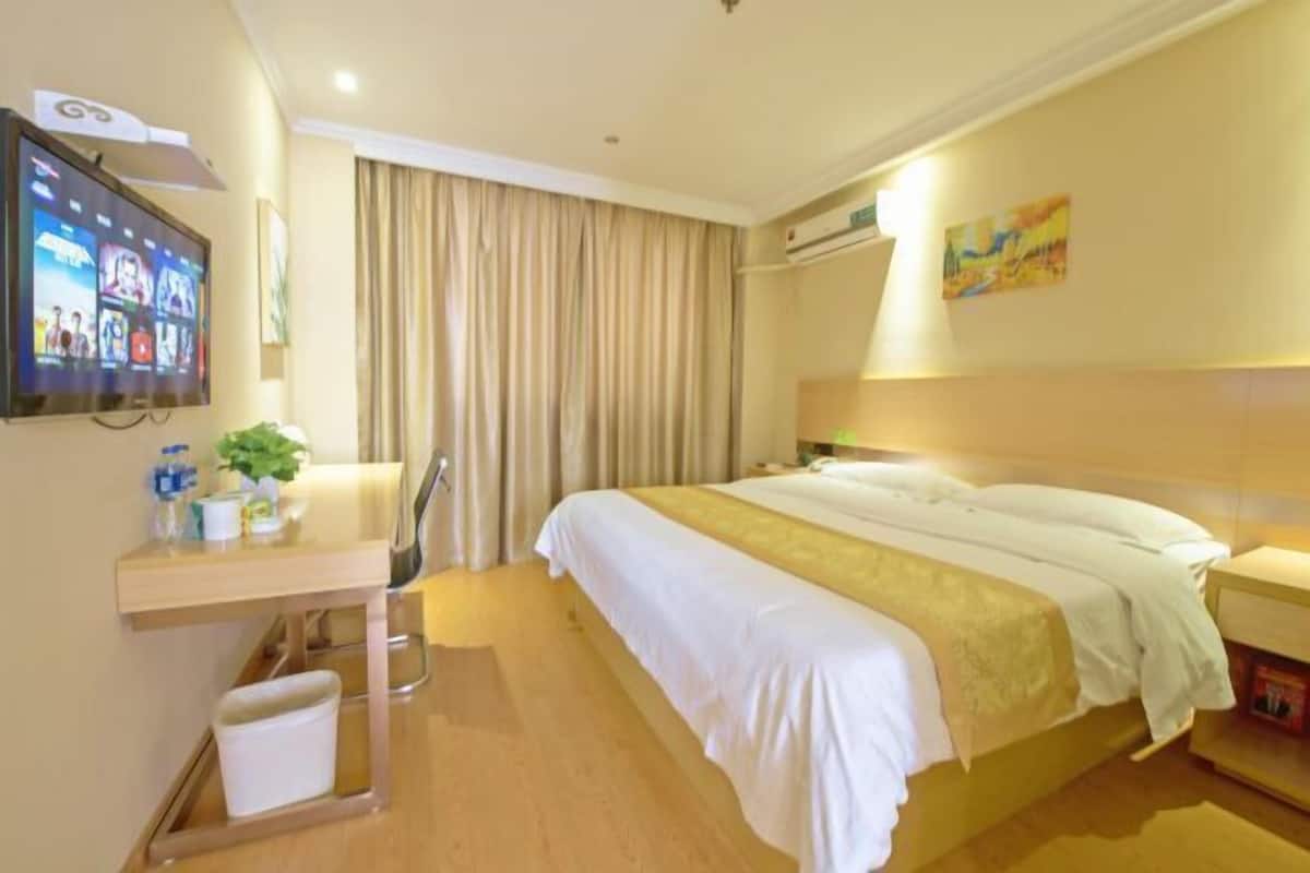 Una habitación de hotel con cama, escritorio y silla, televisor y ventana con cortinas.