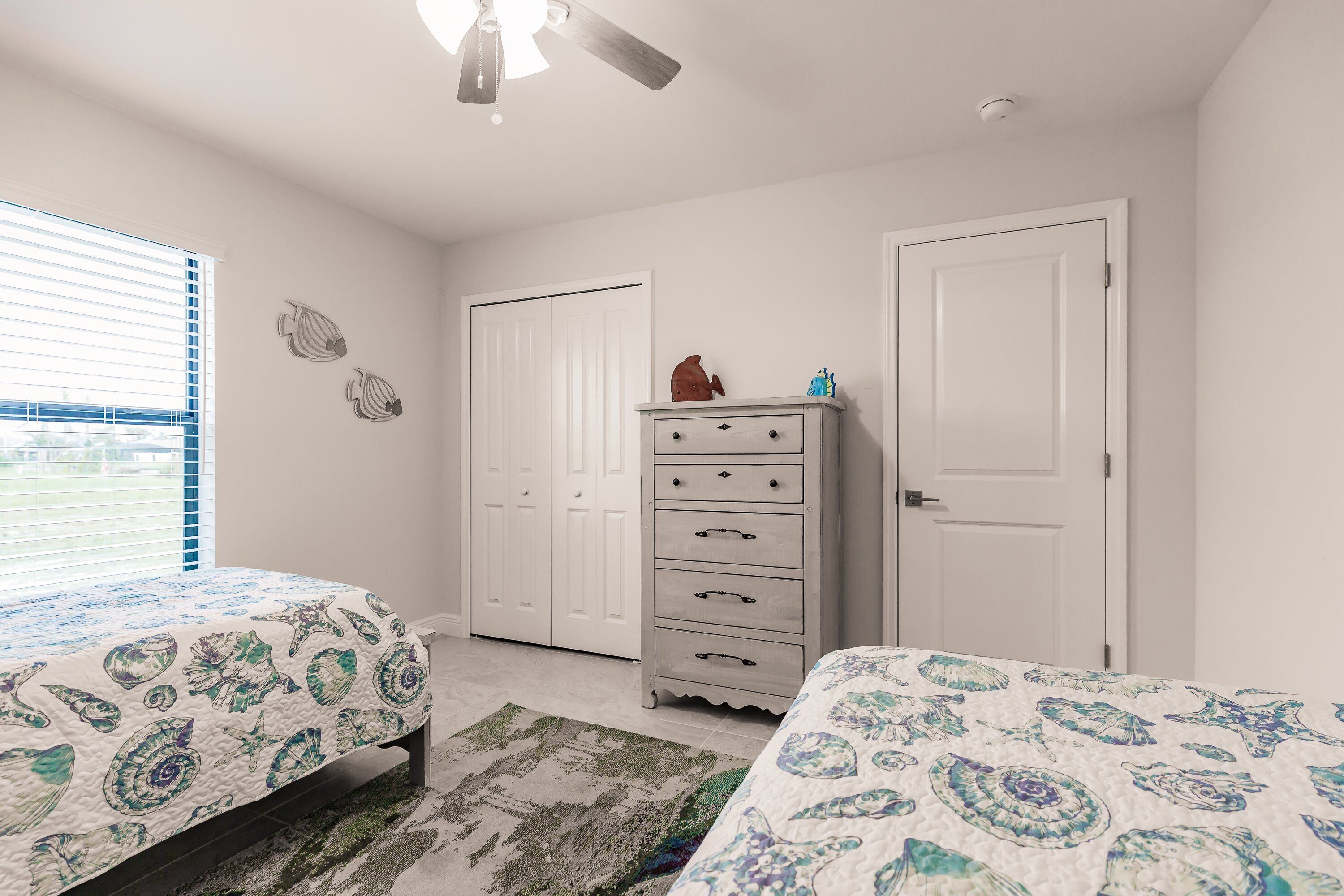 A bedroom with two beds, a dresser, and a ceiling fan.