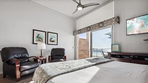 Ein Schlafzimmer mit einem großen Bett, zwei Ledersesseln, einem Deckenventilator und Meerblick durch eine Schiebetür.
