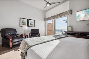 A bedroom with a large bed, two leather chairs, a ceiling fan, and a view of the ocean through a sliding door. - OCEAN FRONT STUDIO ON THE SAND! (Carlsbad)