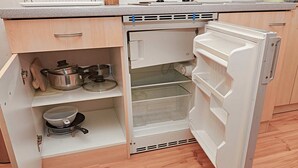 A compact kitchen with a built-in refrigerator, wooden cabinets, and a small cooking area with pots and a strainer. - VILA RHEA - Ubytovanie Vysoke Tatry (Vazec)