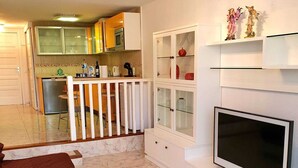 A living room with a TV, a glass coffee table, a sofa, and a kitchen in the background. - Parque Santiago 2. 2 bedroom 3 bathroom duplex. (Arona)