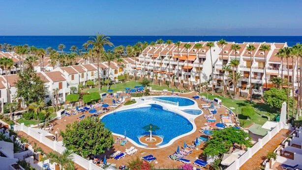 A resort with a central pool surrounded by sun loungers and umbrellas, multiple buildings with balconies, and a view of the ocean. - Parque Santiago 2. 2 bedroom 3 bathroom duplex. (Arona)