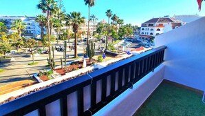 A balcony with a view of a parking lot, palm trees, and buildings in the background. - Parque Santiago 2. 2 bedroom 3 bathroom duplex. (Arona)