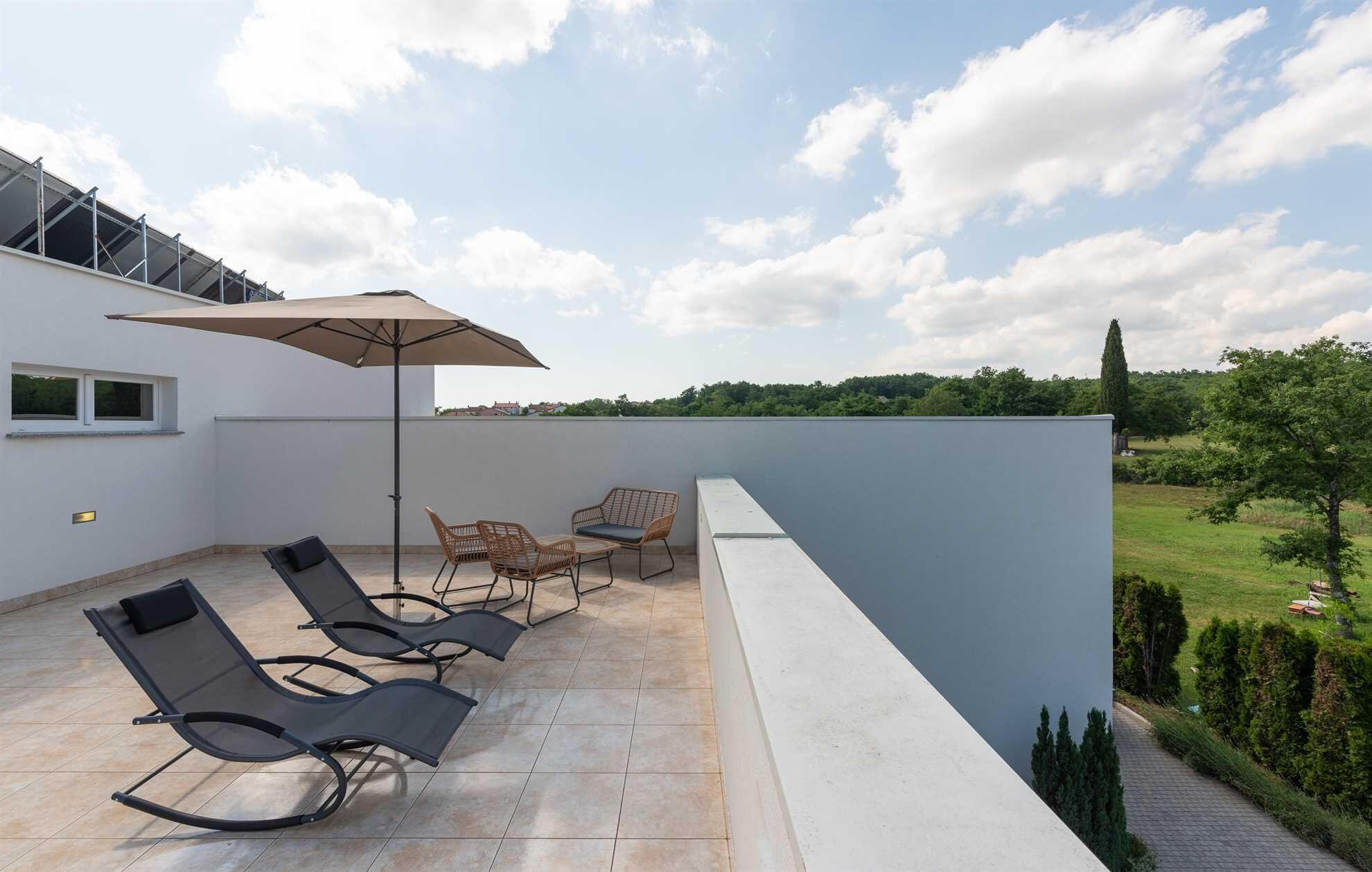 Une terrasse sur le toit, avec des chaises longues, une table et un parasol.