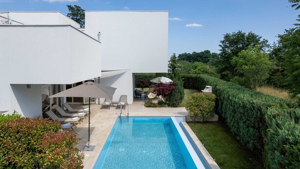 Ein modernes Haus mit Swimmingpool, Sitzgelegenheit im Freien und einem gepflegten Garten.