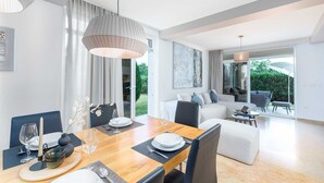 Ein moderner Essbereich mit Holztisch, gedecktem Tisch für eine Mahlzeit, einer Couch und Blick auf den Garten durch große Fenster.