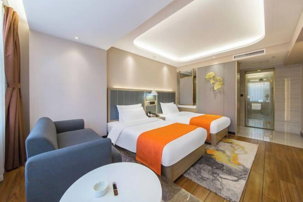 A hotel room with two beds, a sofa, a small table, and a bathroom with a glass door.