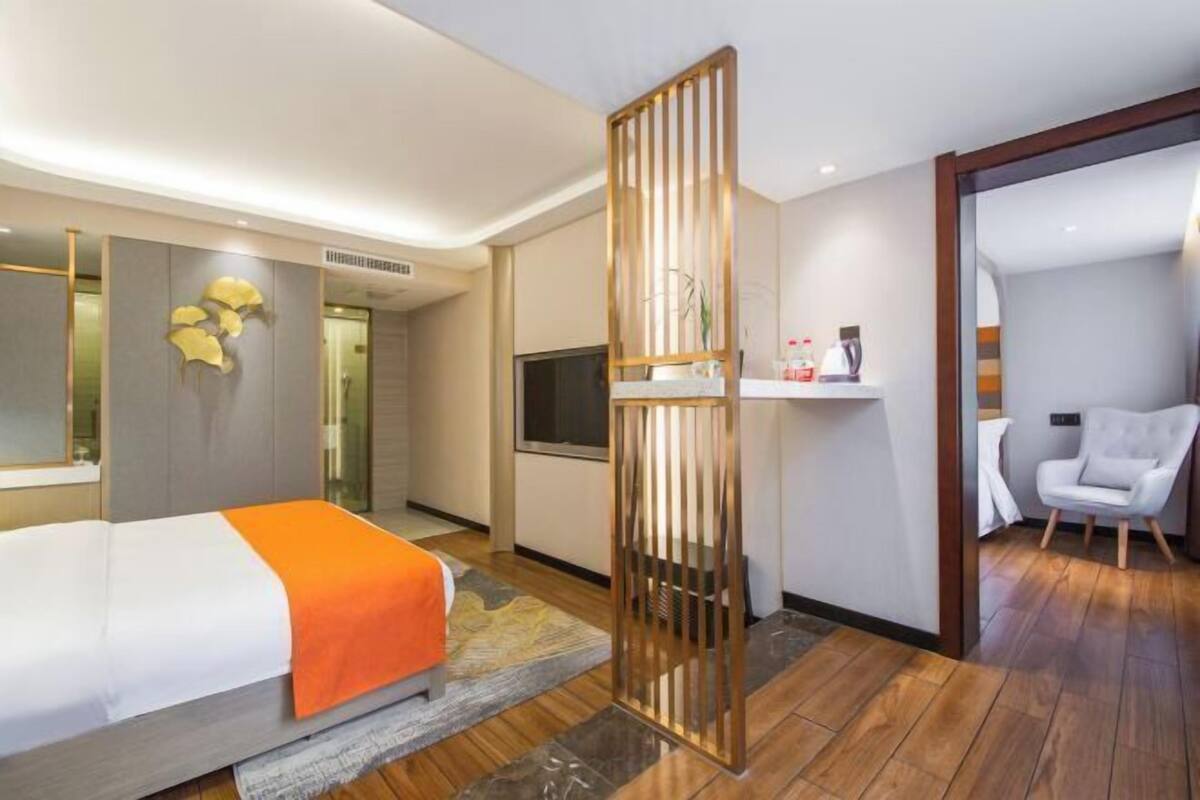 A modern hotel room with a bed, a TV, a desk with a chair, and a decorative partition.