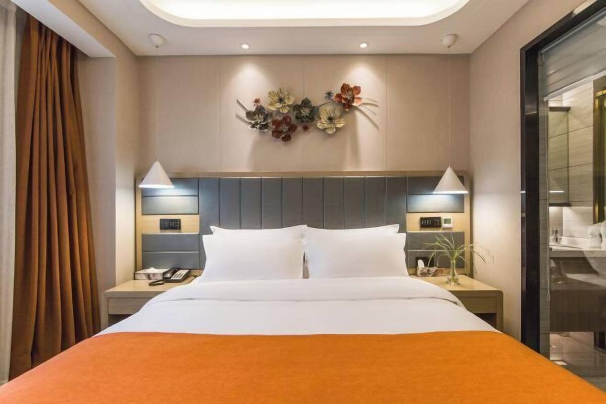 A hotel room with a bed, nightstands, a wall-mounted light fixture, and a decorative wall piece.