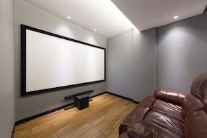 A modern home theater room with a large flat-screen TV mounted on the wall, a leather sofa, and a wooden floor.