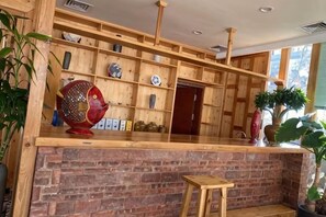 Un espace d’accueil avec un comptoir en bois, des étagères ornées d’objets décoratifs et un mur en briques.
