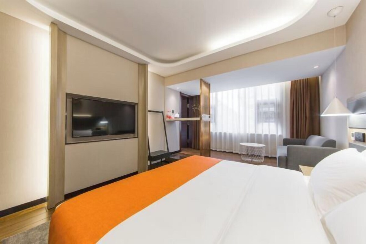 A hotel room with a bed, a TV, a desk, and a window with curtains.