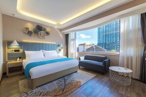 A modern hotel room with a large bed, a sofa, a round coffee table, and a view of a cityscape through large windows. - Huaxi Hongta Avenue High-speed Railway Station (Yuxi)