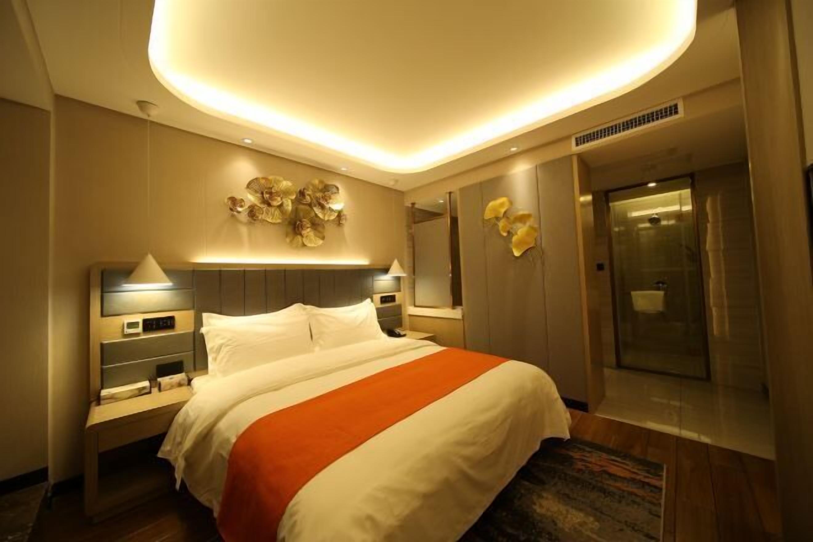 Une chambre d’hôtel comprenant un lit, des tables de chevet, une horloge murale, un miroir et une porte donnant accès à une salle de bain.