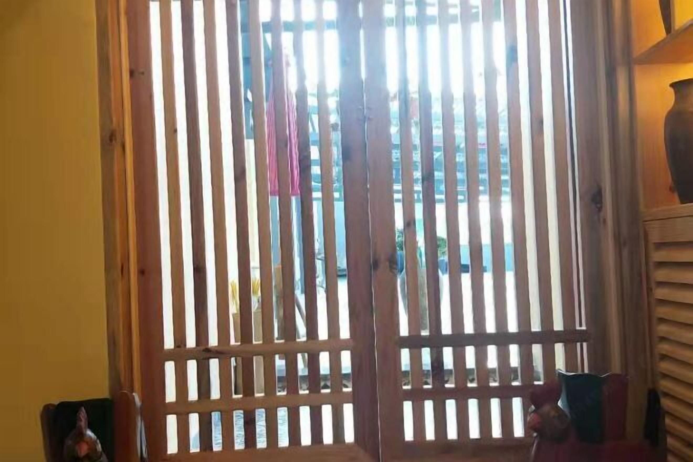 A room with a wooden slatted window, a small table with a vase, and a chair.