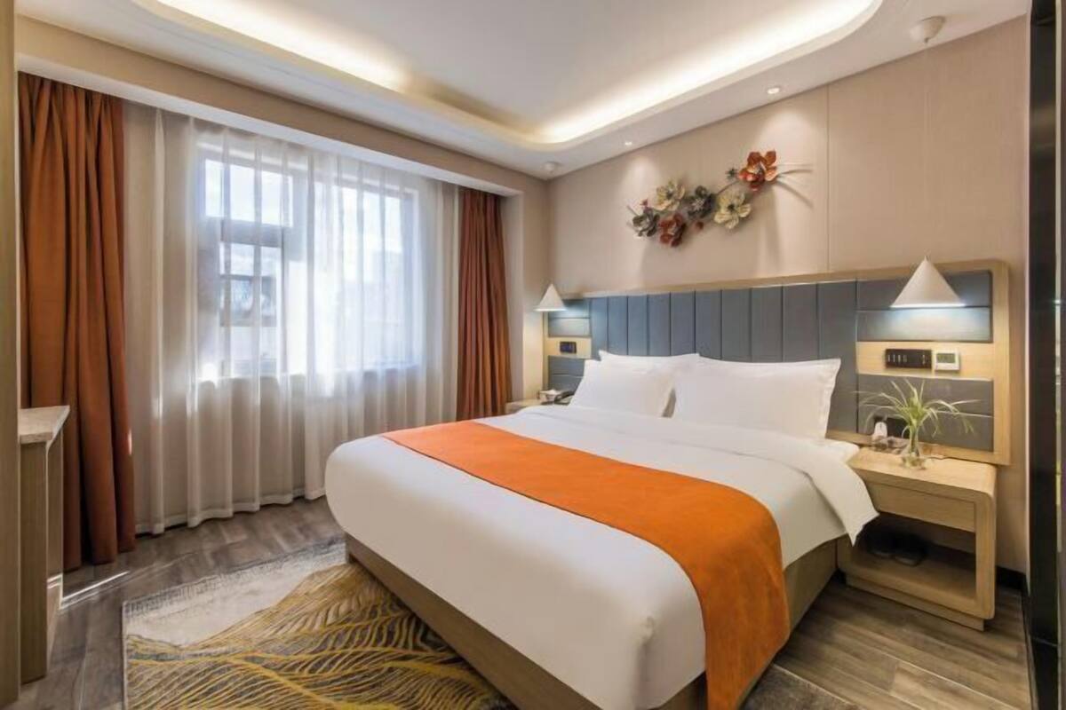 A hotel room with a large bed, a nightstand, a wall-mounted clock, and a window with curtains.