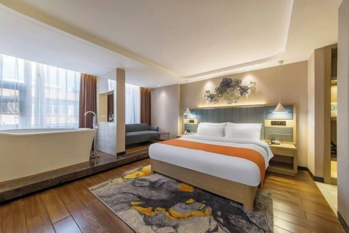 A hotel room with a large bed, a bathtub, a sofa, a desk, and a wall-mounted artwork.